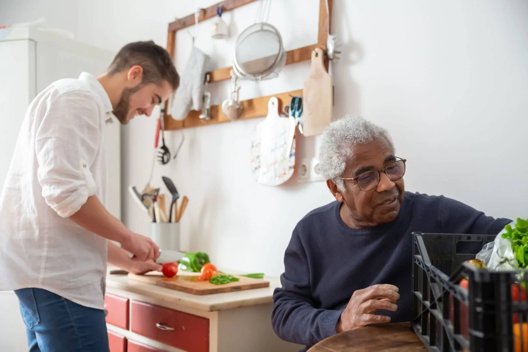 Older man and younger man preparing vegetables together in a modest home kitchen